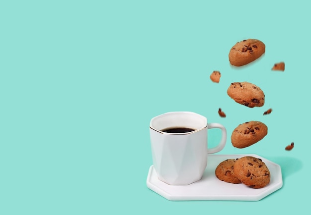 Foto taza blanca de café negro sobre fondo de menta con apetitosas galletas y migas, elevándose en el aire.