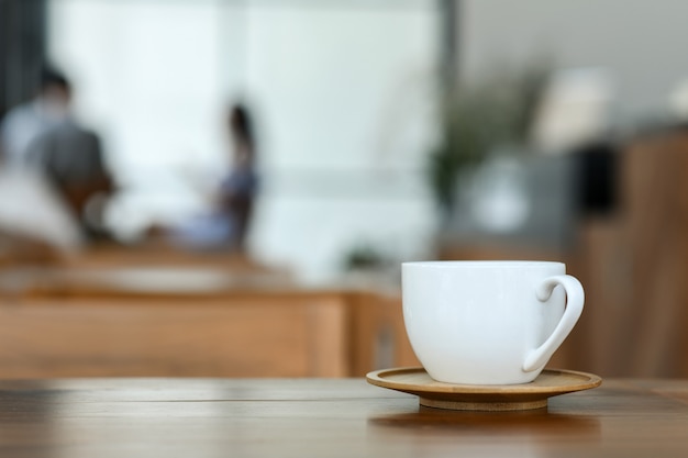 Taza blanca del café en piso de madera en café.