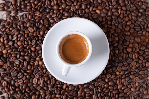 Taza blanca con café en un plato blanco en el centro de los granos de café