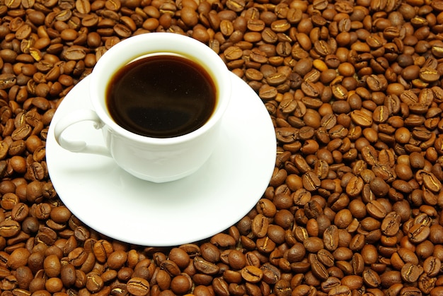 Taza blanca con café que cuesta en un grano de café