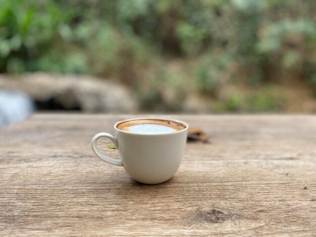 Una taza blanca de café se sienta en una mesa de madera frente a un fondo borroso.