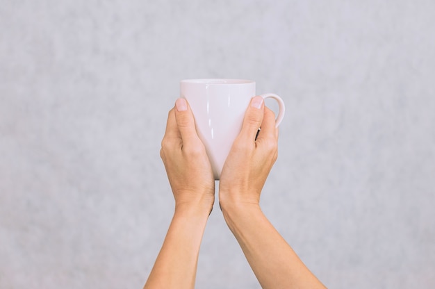 Taza blanca para café, té en manos de una niña. Sobre un fondo blanco.