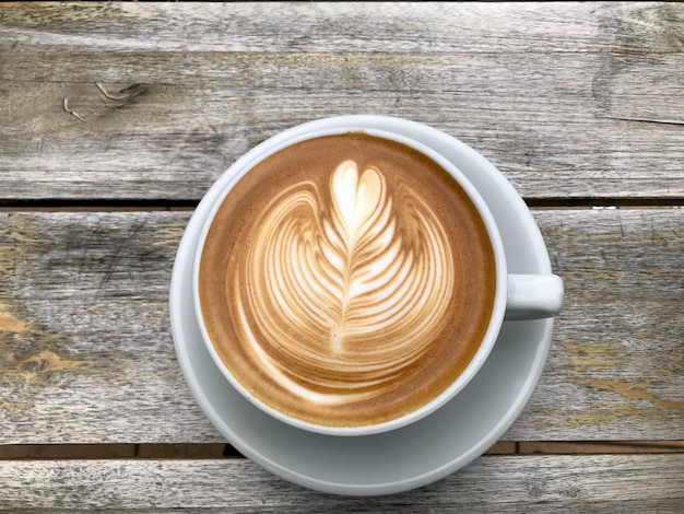 Una taza blanca de capuchino con arte latte sobre fondo de mesa de madera