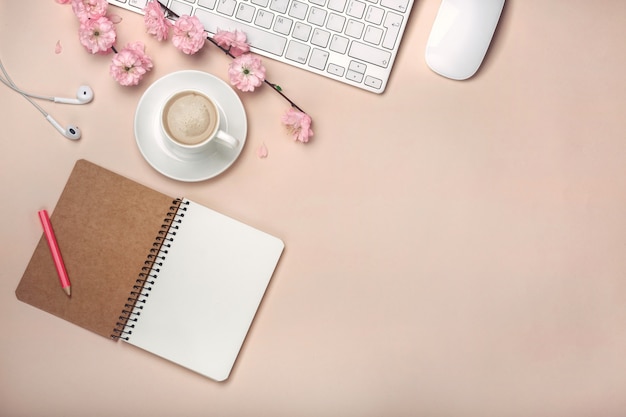 Taza blanca con capuchino, flores de sakura, teclado, reloj despertador, cuaderno.