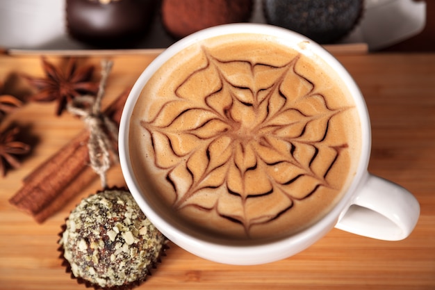 Foto taza blanca de capuchino con un patrón de latte-art en forma de una flor. café, pastel, canela, anís, mesa de madera.