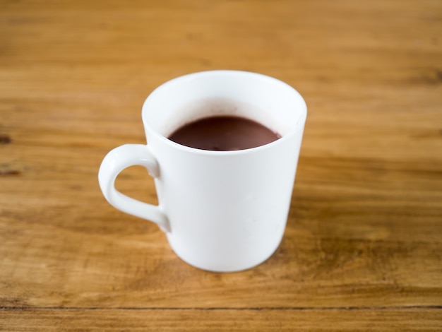 La taza blanca de chocolate caliente o café sirvió en la tabla de madera.