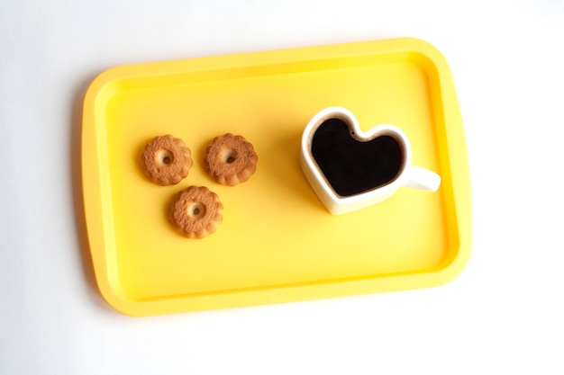 Taza blanca en forma de corazón con café y galletas en una bandeja amarilla, vista superior