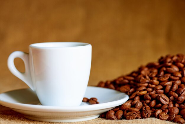 Taza blanca y granos de café en borrosa.