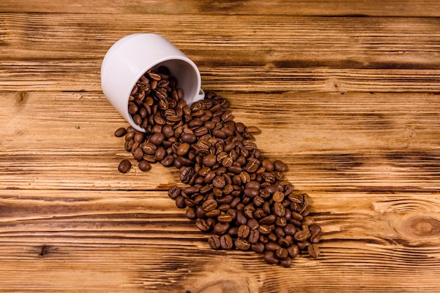 Taza blanca y granos de café esparcidos sobre una mesa de madera rústica