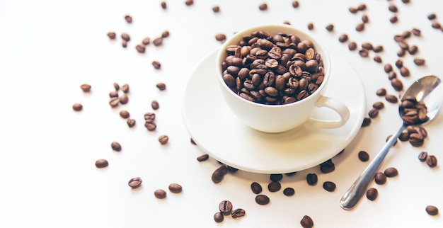 Taza blanca y granos de café sobre un fondo blanco. Enfoque selectivo.