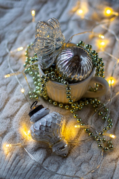 Taza blanca llena de adornos navideños a la luz de una guirnalda