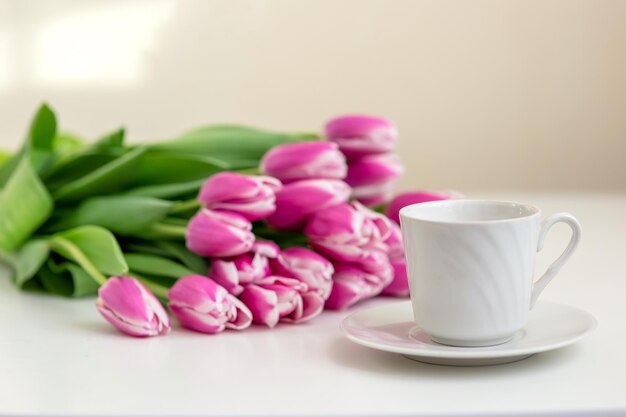 Una taza blanca con un platillo y un ramo de hermosos tulipanes rosados