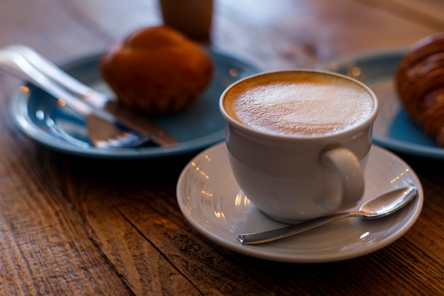 Taza blanca de primer plano de capuchino con bollo en el fondo