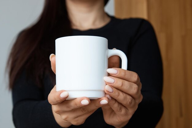 Taza blanca para té y café en las manos de una chica de primer plano