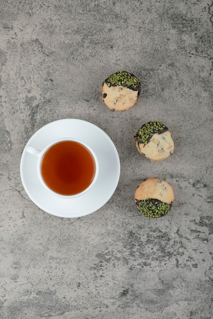 Una taza blanca de té caliente con deliciosas galletas colocadas sobre la mesa de piedra.