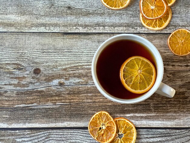 Taza blanca de té con chips de naranja y naranja esparcidos sobre un fondo de madera, vista superior