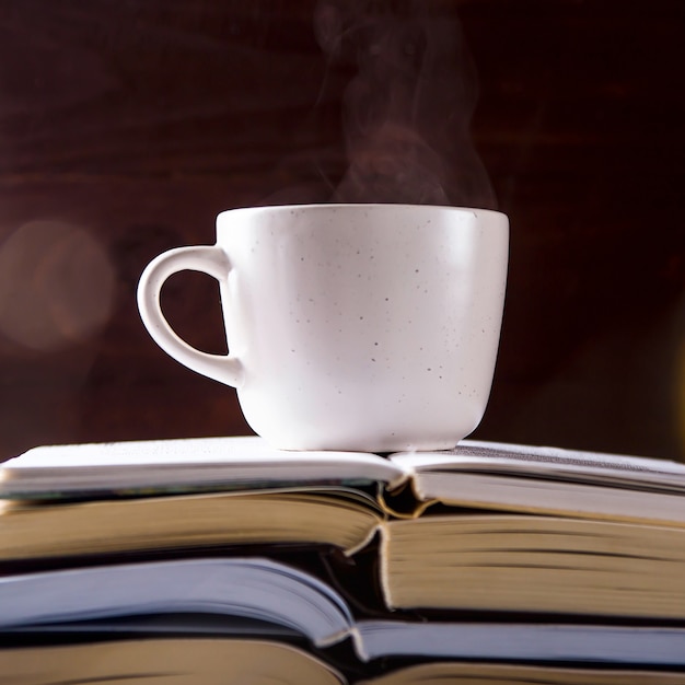 Una taza blanca con té está en la pila abierta de libros