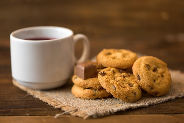 Taza blanca de té y galletas sobre fondo de madera oscura.