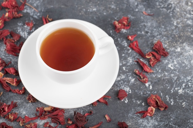 Taza blanca de té negro caliente con capullos secos colocados sobre una mesa gris oscuro.