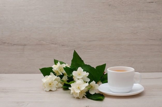 Taza blanca con té, una rama de jazmín en la madera