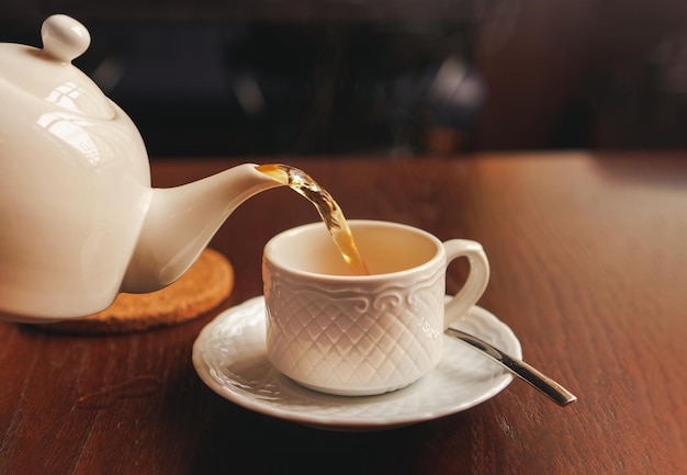 Taza blanca con tetera La mano que sostiene la tetera vierte el té en una olla de pie en el platillo