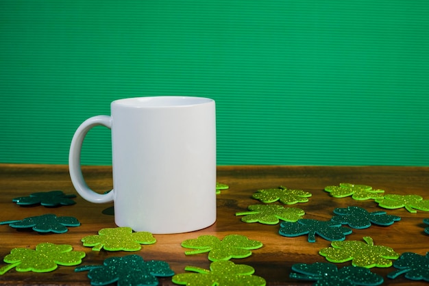 Taza blanca con tréboles con purpurina alrededor de la mesa de madera Fondo verde