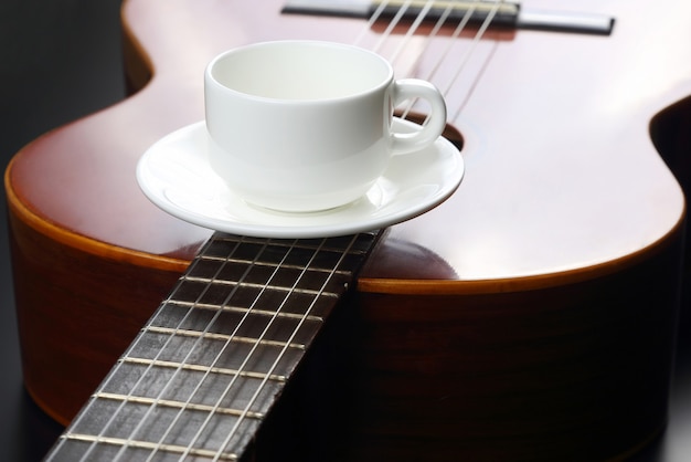 Taza blanca vacía sobre la guitarra acústica