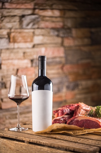 Taza y una botella de vino tinto y bistec de ternera cruda en la mesa de madera.