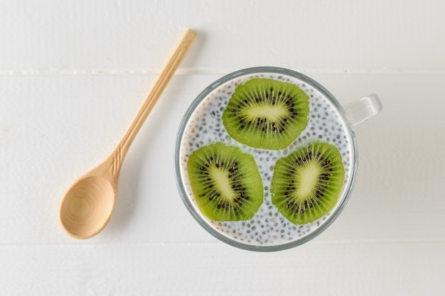 Una taza de budín de semillas de Chia negro y tres rodajas de kiwi sobre una mesa de madera blanca. La vista desde la cima. Endecha plana.