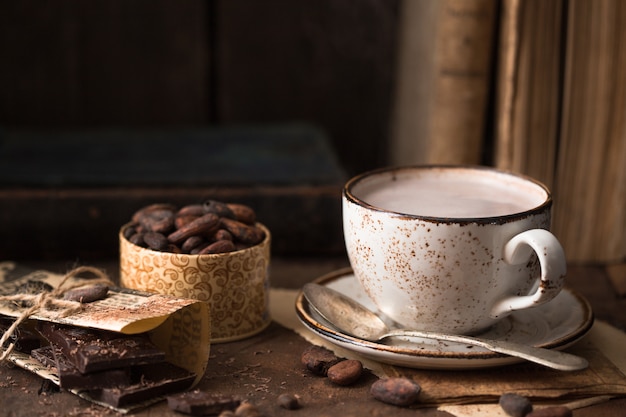 Taza de cacao aromático en mesa vieja con granos de cacao