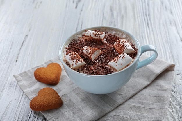 Taza de cacao caliente con malvavisco y galletas en forma de corazón en una servilleta de algodón de cerca