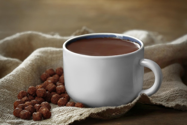 Taza de cacao con dulces y servilleta sobre mesa de madera