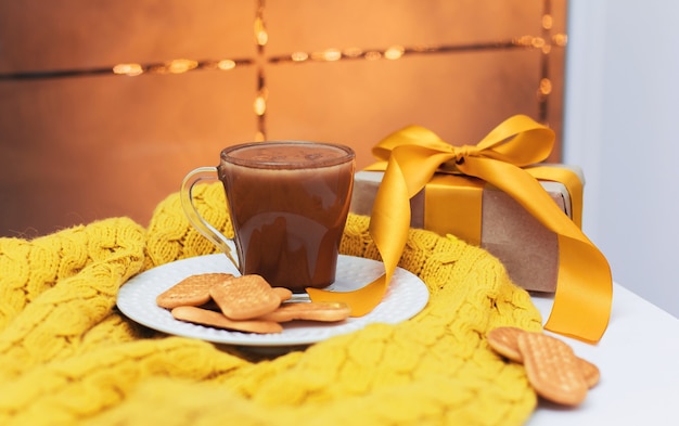 Una taza de cacao y galletas en una placa blanca sobre una mesa blanca y una manta tejida amarilla