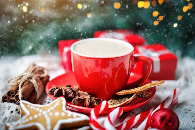 Taza de cacao, galletas, regalos y ramas de abeto en una mesa de madera blanca