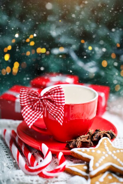 Taza de cacao, galletas, regalos y ramas de abeto en una mesa de madera blanca