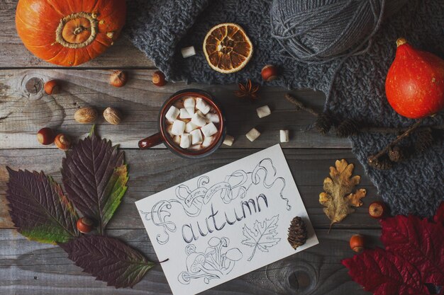 Taza de cacao con malvavisco postal de otoño casera hojas de otoño calabaza y nueces sobre fondo de madera rústica imagen de otoño cálida y acogedora vista superior de naturaleza muerta estacional enfoque selectivo tonificado