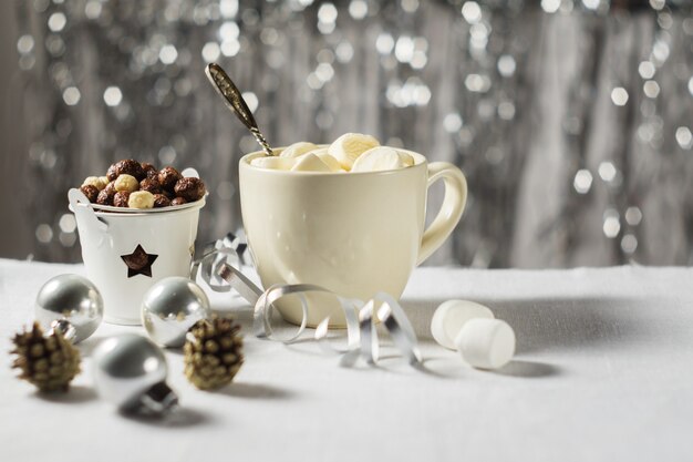 Una taza de cacao con malvaviscos y bolas de maíz en la mesa de Navidad de Año Nuevo sobre un fondo brillante