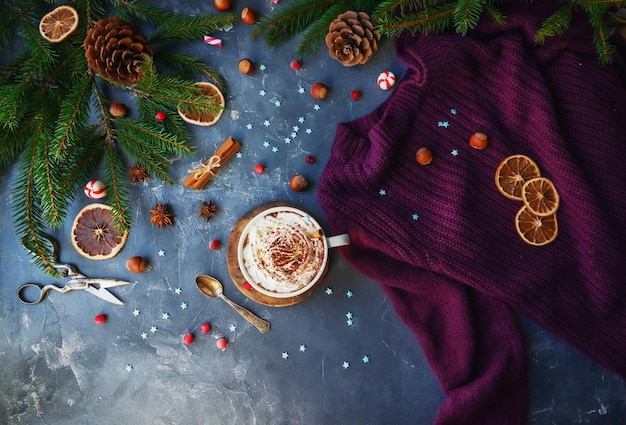 Foto taza de cacao o chocolate caliente con crema de canela, naranjas secas, suéter cálido y abeto en la mesa de piedra oscura, decoración navideña, acogedor fondo de casa de invierno, vista superior, enfoque selectivo