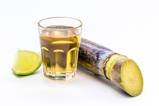 Taza de cachaÃ§a brasileña sobre fondo blanco aislado con caña de azúcar en el lateral.