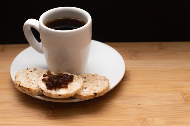 Foto taza de café al lado de un arroz, galletas veganas con gelatina en la parte superior debajo de la mesa de madera