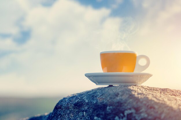 Taza de café amarilla en piedra contra el cielo nublado Espacio para texto