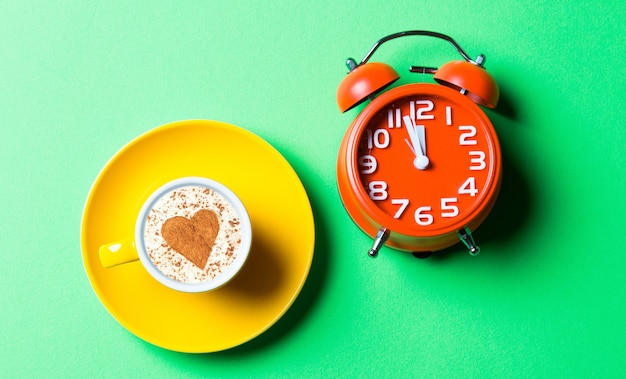 Taza de café amarilla y reloj rojo en el verde