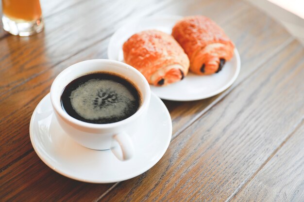 Foto taza de café americano con panadería servido en mesa de madera.