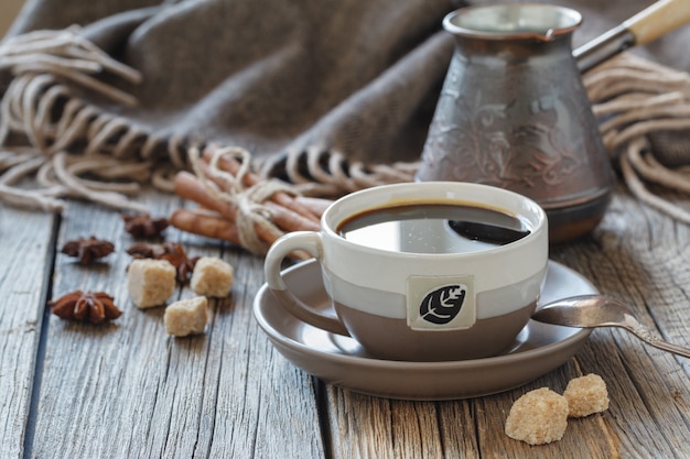 Taza de café con azúcar y especias y una caja de madera con granos de café sobre una tabla de madera