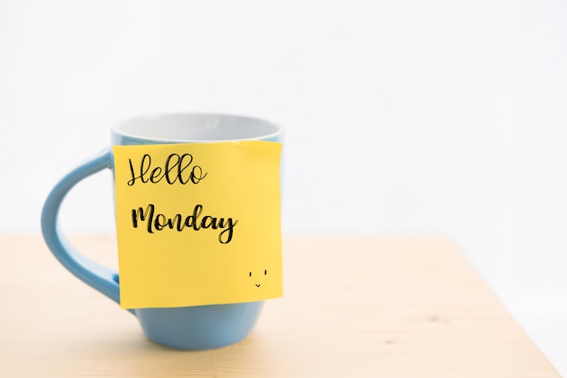 Taza de café azul y nota adhesiva con el mensaje "Hola lunes", en la mesa de madera