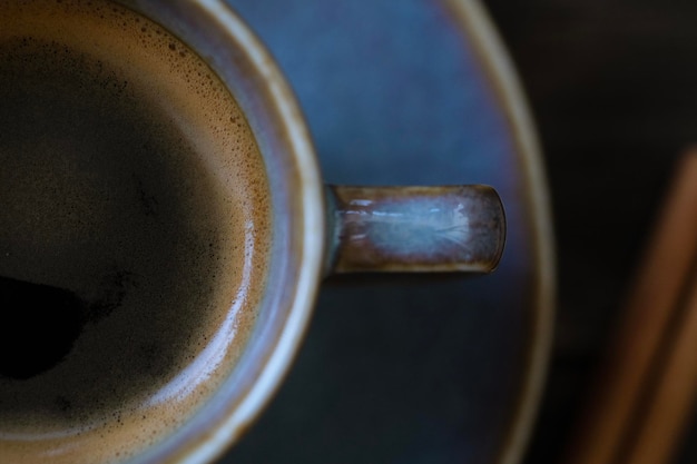 Taza de café azul con platillo y palitos de canela sobre fondo de madera