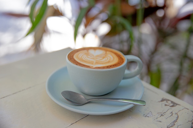 Taza de café azul sobre fondo blanco rústico con hermoso arte latte