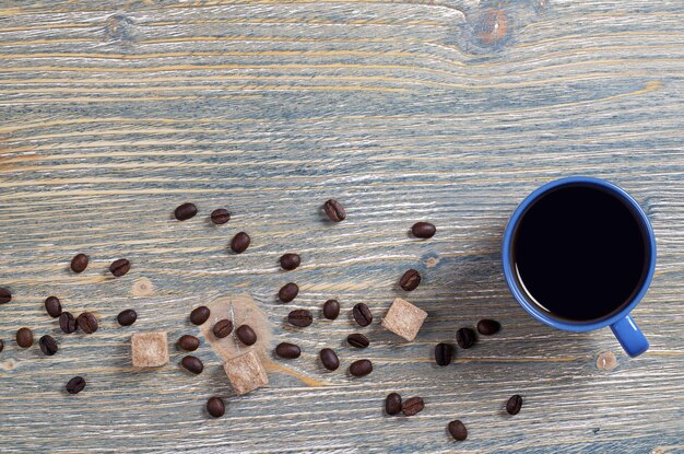 Taza de café azul con terrones de azúcar y frijoles sobre fondo de madera vieja, vista superior con espacio para texto