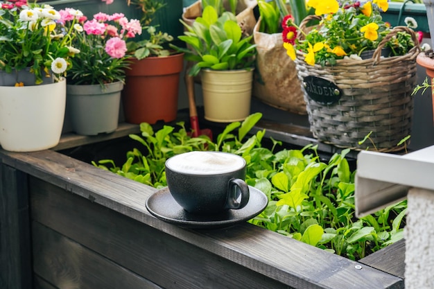 Taza de café en el balcón entre plantas verdes y flores