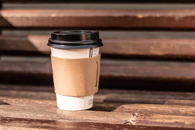 Una taza de café en el banco de madera en el parque de la calle